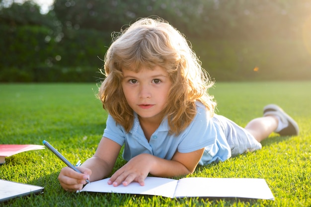 Lindo niño encantador con lápiz escribiendo en el cuaderno fuera del niño leer un libro en el parque casa de vacaciones de verano ...