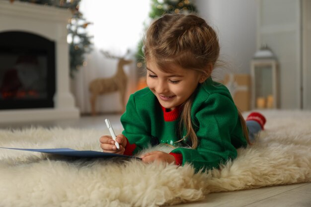 Lindo niño escribiendo carta a Santa Claus en casa tradición navideña