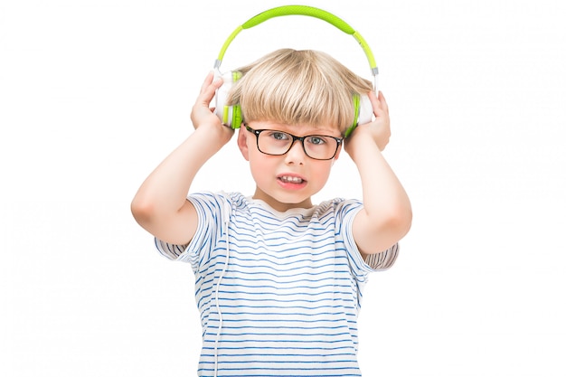 Lindo niño escuchando la música muy alta con auriculares o auriculares. Niño infeliz aislado sobre fondo blanco escuchando la radio.