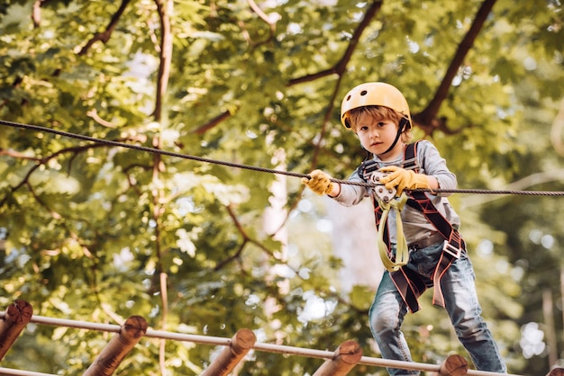 Lindo niño de la escuela disfrutando de un día soleado en un parque de actividades de aventura de escalada