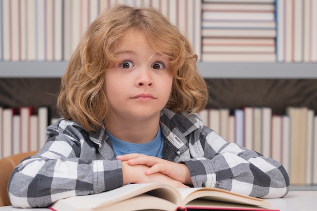 Lindo niño de la escuela estudiando en la biblioteca de la escuela Retrato de niño leyendo en la biblioteca en el fondo con libros