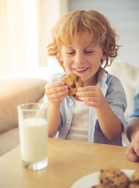 Lindo niño está sonriendo, bebiendo leche y comiendo galletas