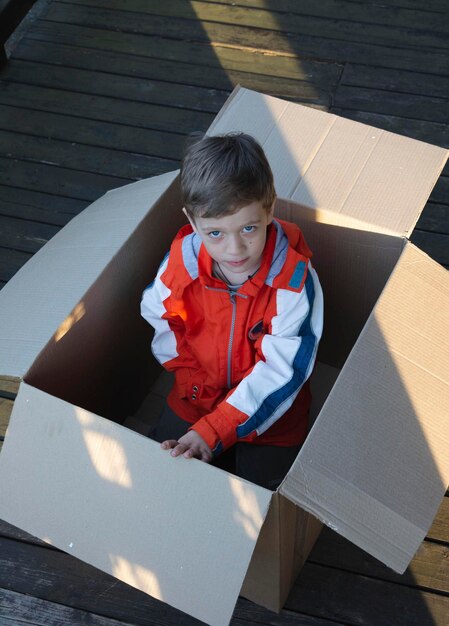 Lindo niño europeo asomándose por una caja de cartón regalo sorpresa vida sin hogar embalaje ocultar