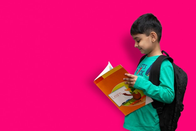 Lindo niño feliz de 7 años con mochila escolar sosteniendo libros en fondo liso para el concepto de educación