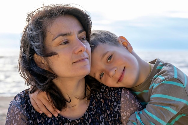 Lindo niño feliz abraza a su madre junto al mar mirando a la cámara