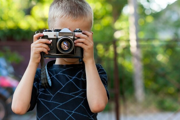 Lindo niño feliz con cámara de fotos vintage al aire libre