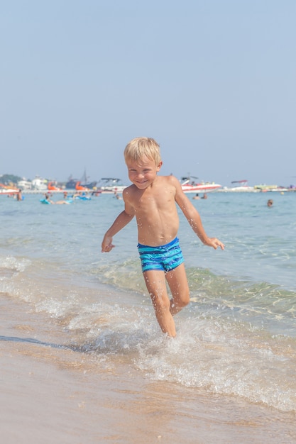 Lindo niño feliz divertido jugando en las olas del agua en el mar océano en un día soleado