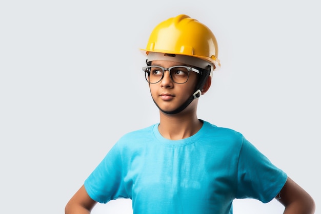 Lindo niño feliz indio asiático con casco de construcción amarillo o casco de seguridad, que se encuentran aisladas en la pared blanca con plano