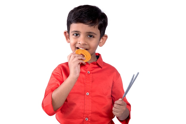 Lindo niño indio comiendo murukku o chakli sobre una pared blanca