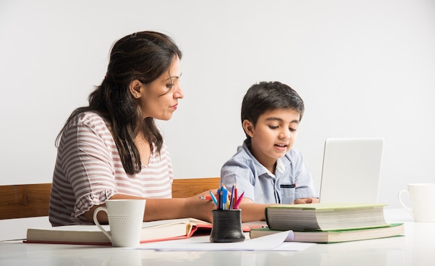 Lindo niño indio con madre haciendo los deberes en casa usando laptop y libros - concepto de escolarización en línea