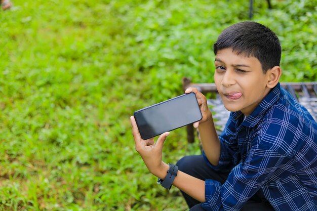 Lindo niño indio mostrando smartphone con pantalla en blanco