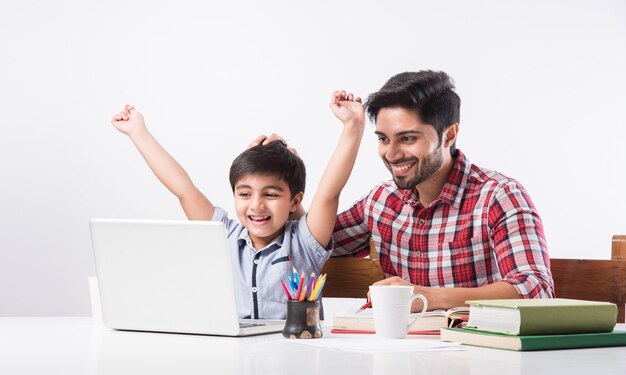 Lindo niño indio con padre o tutor masculino haciendo la tarea en casa usando laptop y libros - concepto de escolarización en línea