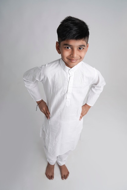 Lindo niño indio en ropa étnica y mostrando expresión sobre fondo blanco.