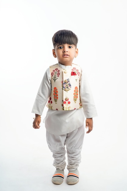 Lindo niño indio en ropa étnica y mostrando expresión sobre fondo blanco.