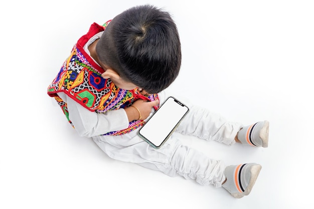 Lindo niño indio con vestido étnico jugando con el teléfono o mostrando la pantalla del teléfono y la expresión en el fondo blanco