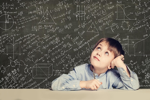 Lindo niño inteligente estudiante en el fondo de la pizarra con fórmulas científicas Concepto de ciencia de aprendizaje