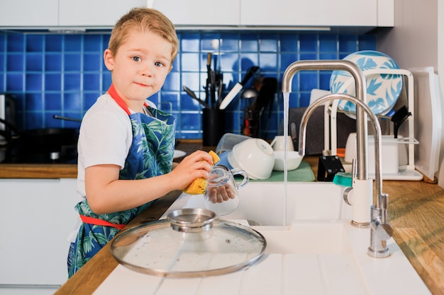 Lindo niño lavando platos en la cocina