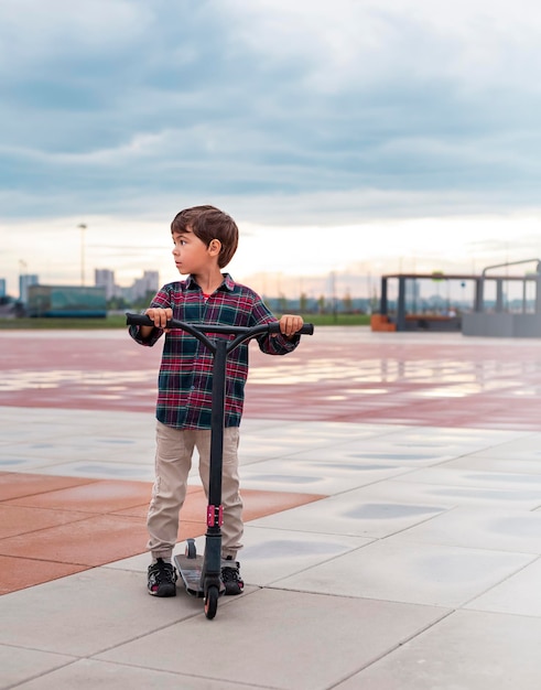 Lindo niño montando scooter en la ciudad Retrato al aire libre