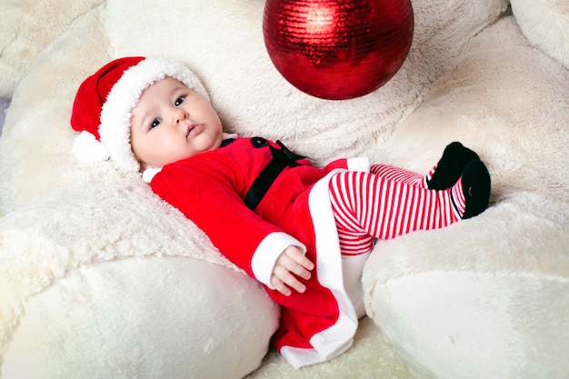 Lindo niño de Navidad en los brazos de un oso de peluche vistiendo traje de santa claus y jugando con juguetes de año nuevo