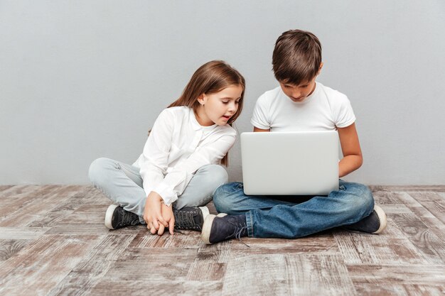 Lindo niño y niña sentados y usando la computadora portátil juntos