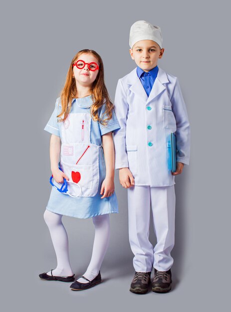 Lindo niño y niña en uniforme médico jugando como médicos