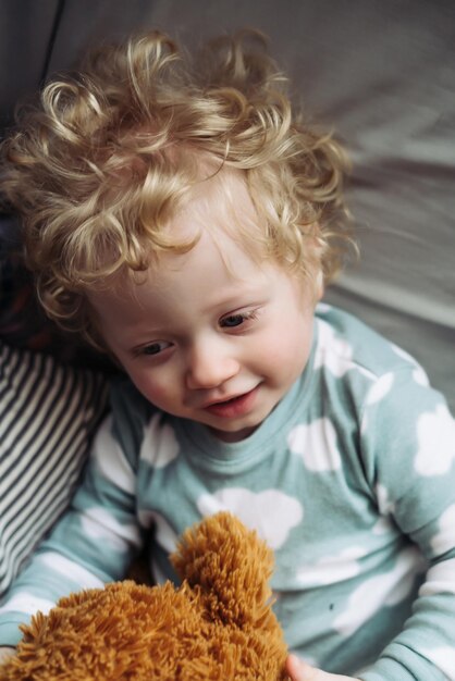 Lindo niño de pelo rizado en pijama azul yace con mamá y sonríe