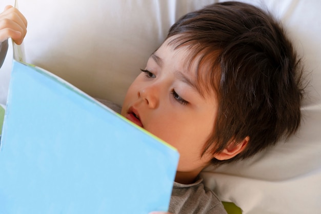 Foto lindo niño pequeño acostado en la cama leyendo un libro antes de irse a dormir