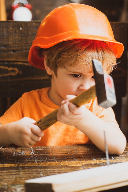 Lindo niño pequeño en casco con tablón de madera y herramientas de carpintero de martillo