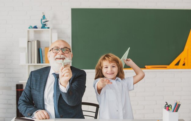 Lindo niño pequeño en clase en la escuela Maestro mayor y en casa trabajando Ancianos entrenador de maestros adolescente alumno niño Día del maestro educación para alumno en la escuela Alumno con avión de papel