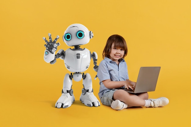 Lindo niño pequeño con computadora portátil sentado en el piso y sonriendo a la cámara adorable niño robot posando cerca