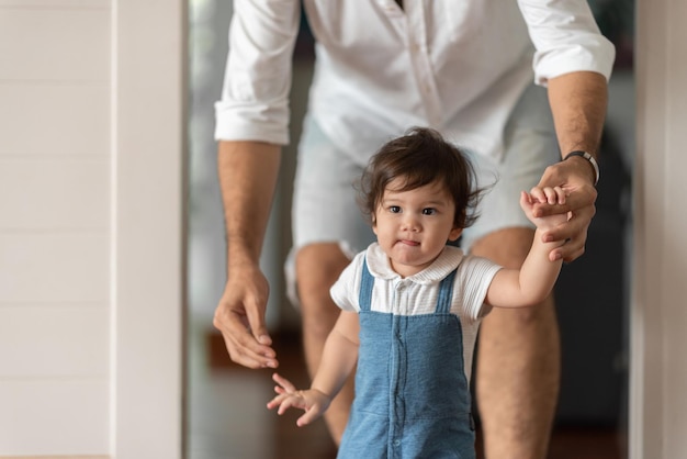 Lindo niño pequeño niño concepto de familia bebé aprendiendo a caminar con el padre y la madre para ayudar a cuidar y tomar de la mano el primer paso con el apoyo de los padres de la infancia pequeño retrato de amor niño pequeño en casa