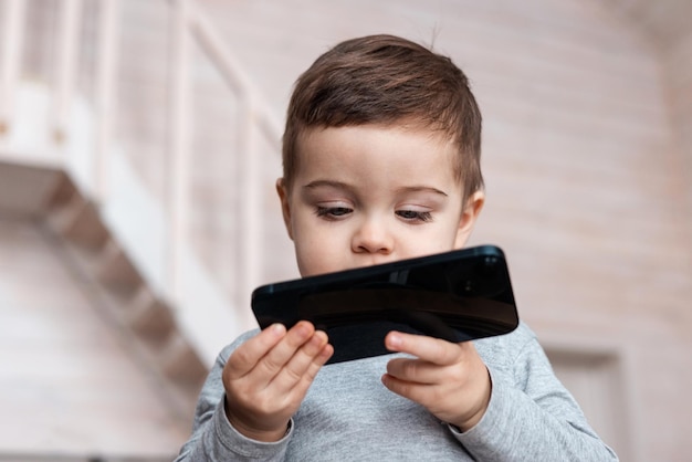 Lindo niño pequeño niño jugando con teléfono inteligente bebé sano tocar el teléfono móvil con los dedos mira ...