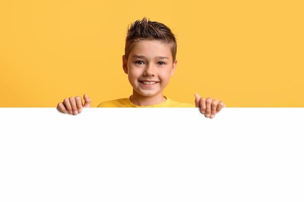 Foto lindo niño pequeño posando detrás de un tablero publicitario en blanco