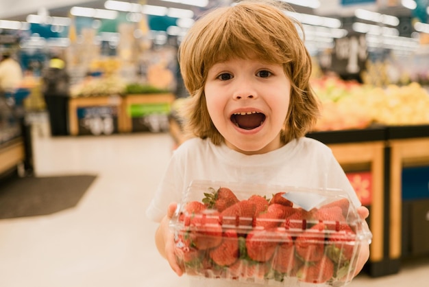 Lindo niño pequeño en una tienda de alimentos o un supermercado eligiendo un estilo de vida saludable de fresa orgánica fresca