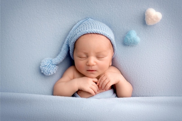 Un lindo niño recién nacido en los primeros días de vida duerme desnudo sobre un fondo de tela azul con un gorro de lana de punto azul Corazón de fieltro azul claro y rosa sobre un fondo azul