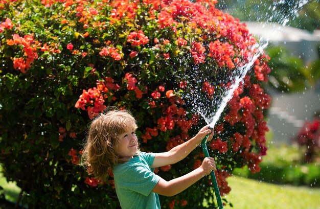 Foto lindo niño regando flores en el jardín en el día de verano niño granjero con manguera de jardín en