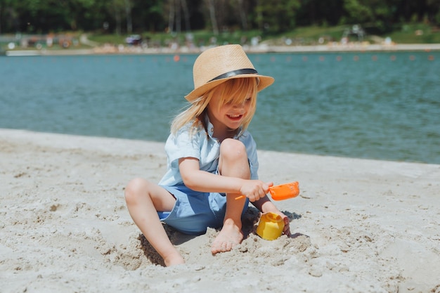 Lindo niño rubio feliz jugando con juguetes de playa en la playa de arena de la ciudad