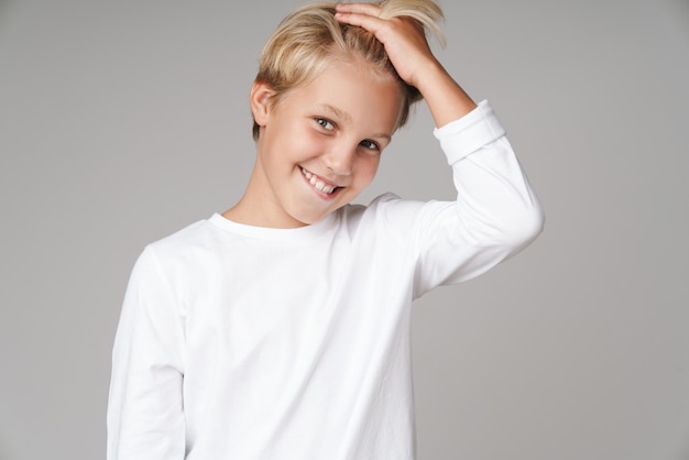 Lindo niño rubio sonriente vistiendo sudadera que se encuentran aisladas sobre la pared gris, mirando