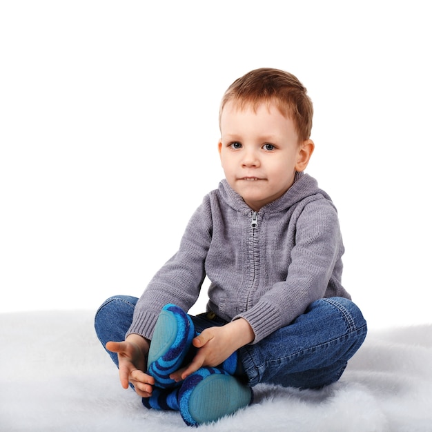 Foto lindo niño sentado en el suelo mordiéndose el labio inferior aislado en blanco
