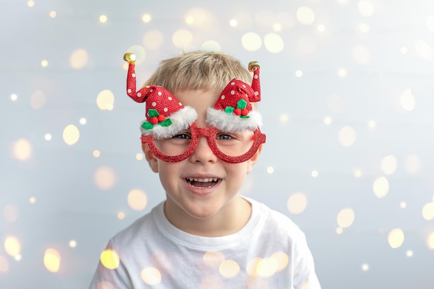 Lindo niño sonriente en gafas de Navidad festivas Fondo claro con bokeh