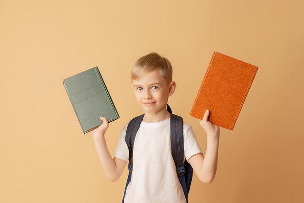 Lindo niño sonriente con una mochila sosteniendo libros en preparación para la escuela sobre un fondo beige