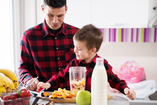 Foto lindo niño y su padre cariñoso están haciendo un batido en una cocina luminosa.