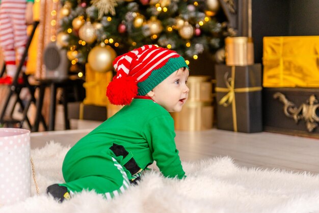 Un lindo niño vestido como un elfo abre un regalo de Navidad en una casa decorada de Navidad.