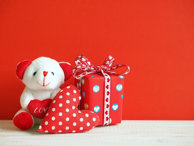 Lindo oso con corazón textil y caja de regalo sobre fondo rojo.