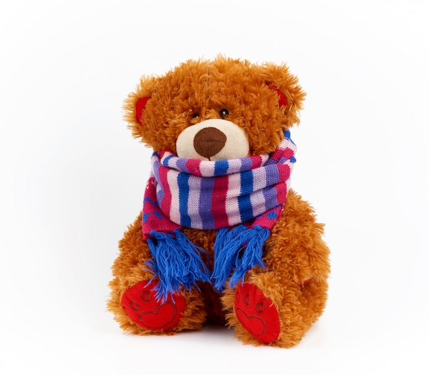 Lindo oso de peluche marrón en una bufanda de punto de color sentado