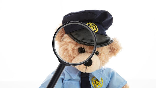 Lindo peluche en uniforme de policía y lupa aislado sobre fondo blanco.