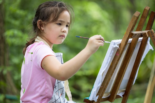 Lindo pequeño artista pintura cuadro pintura sobre lienzo en el bosque de la naturaleza Niña feliz en el jardín