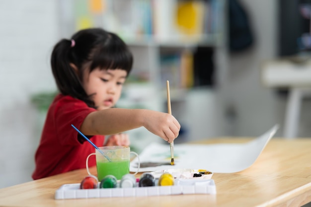 Lindo pequeño bebé asiático sonriendo pintando con pinturas de colores usando acuarela Chica asiática usando pincel de dibujo color Concepto de estilo de vida de actividad de bebé