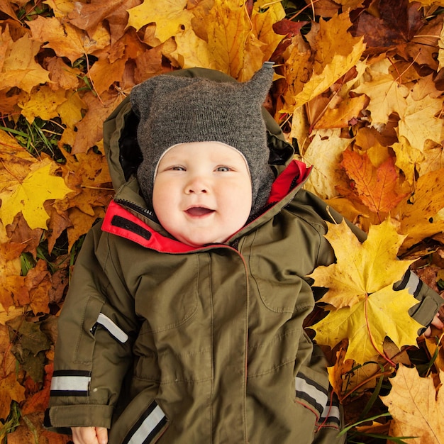 Lindo pequeño bebé en hojas de otoño. Niño feliz (6 meses)