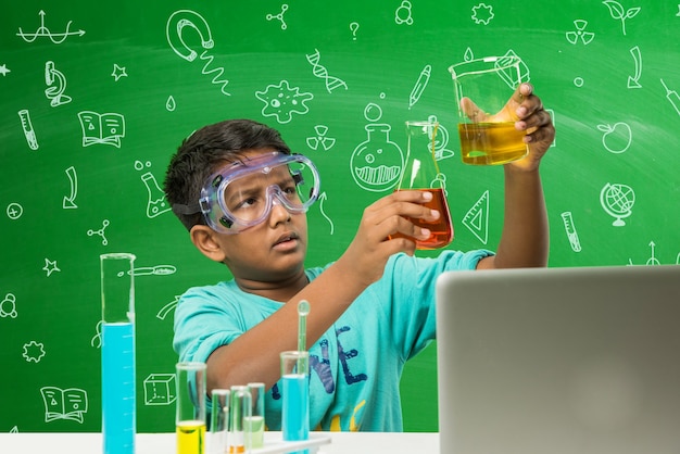 Lindo y pequeño estudiante indio asiático escolar experimentando o estudiando ciencias en laboratorio, sobre fondo de pizarra verde con garabatos educativos